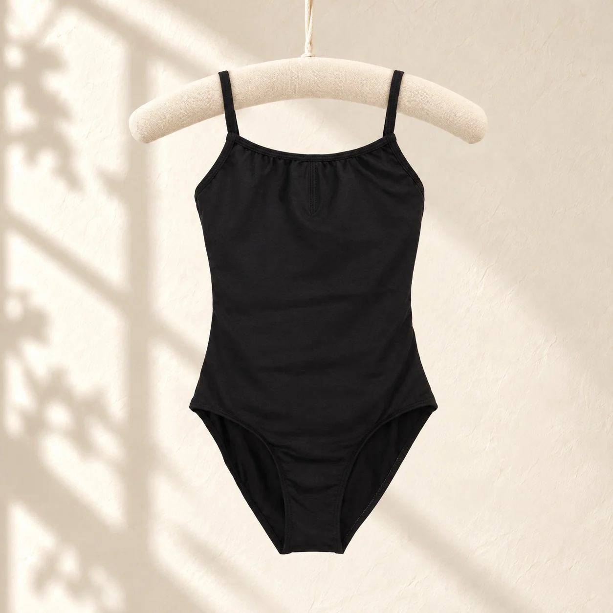 Black thin-strap camisole ballet leotard with a gathered front on a cream hanger