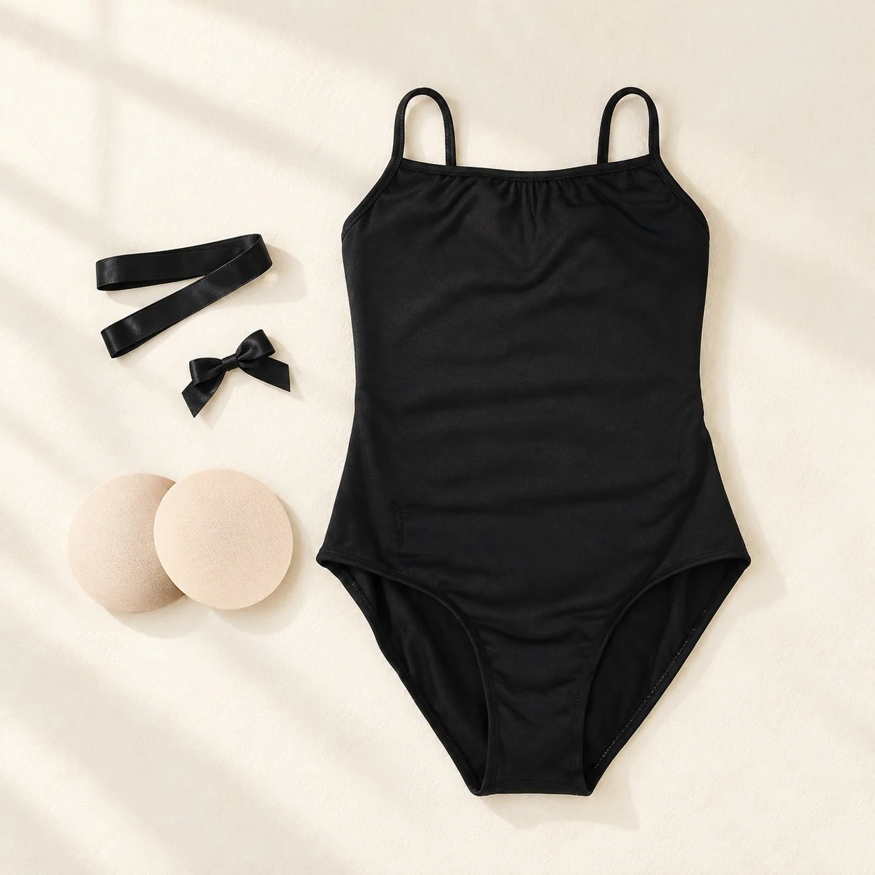 Black camisole leotard laid out with a black waist ribbon, a black bow and a pair of nude chest pads
