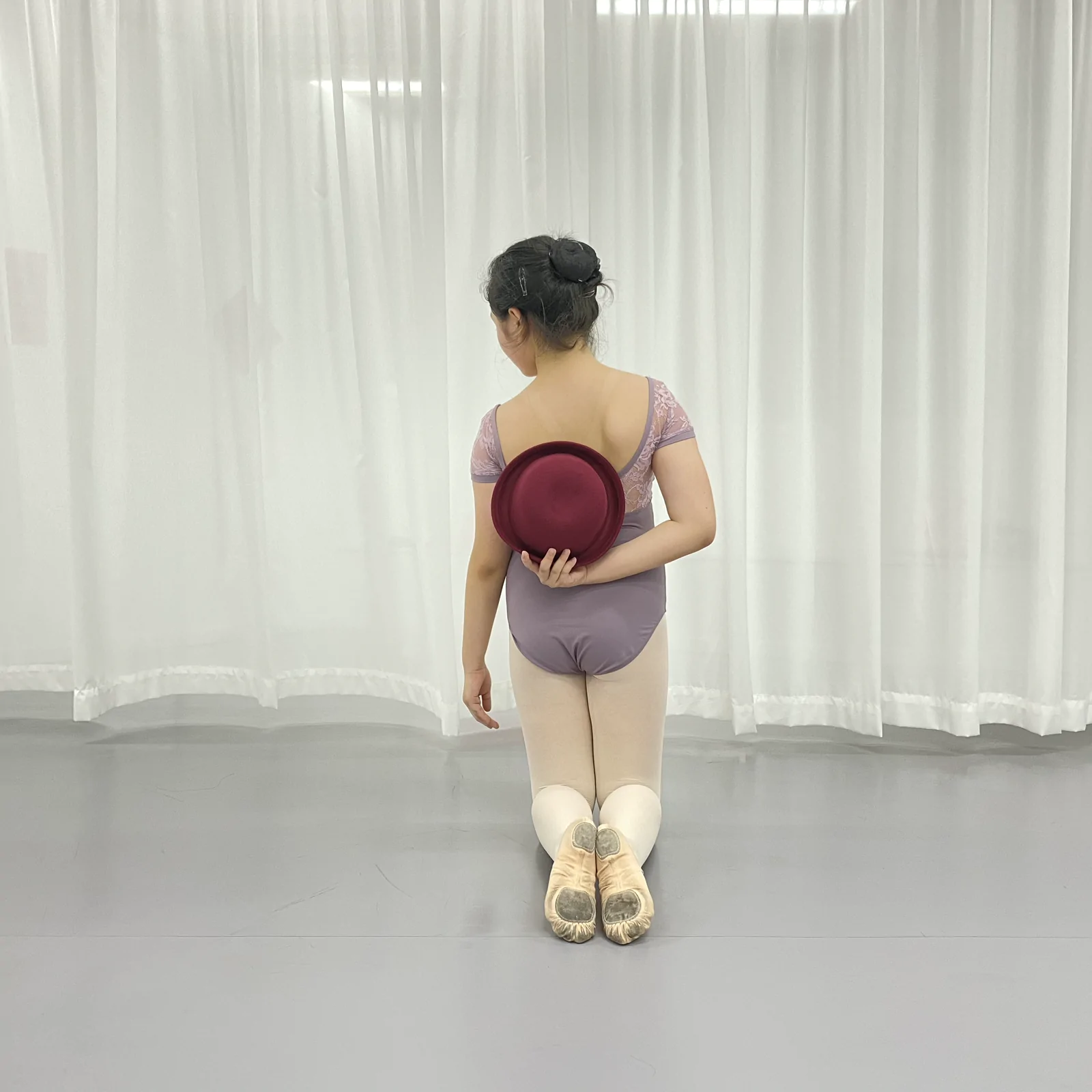 Dancer kneeling in a ballet studio holding the bowler hat behind her back