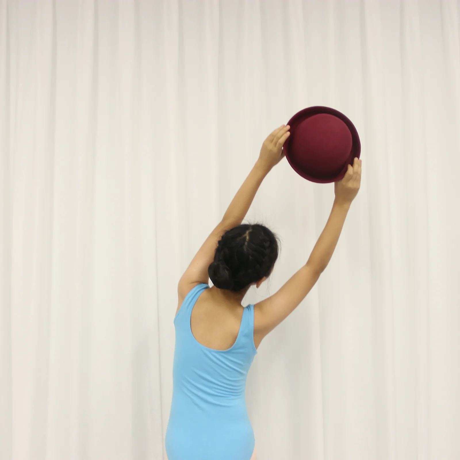 Dancer holding the bowler hat overhead with both arms raised