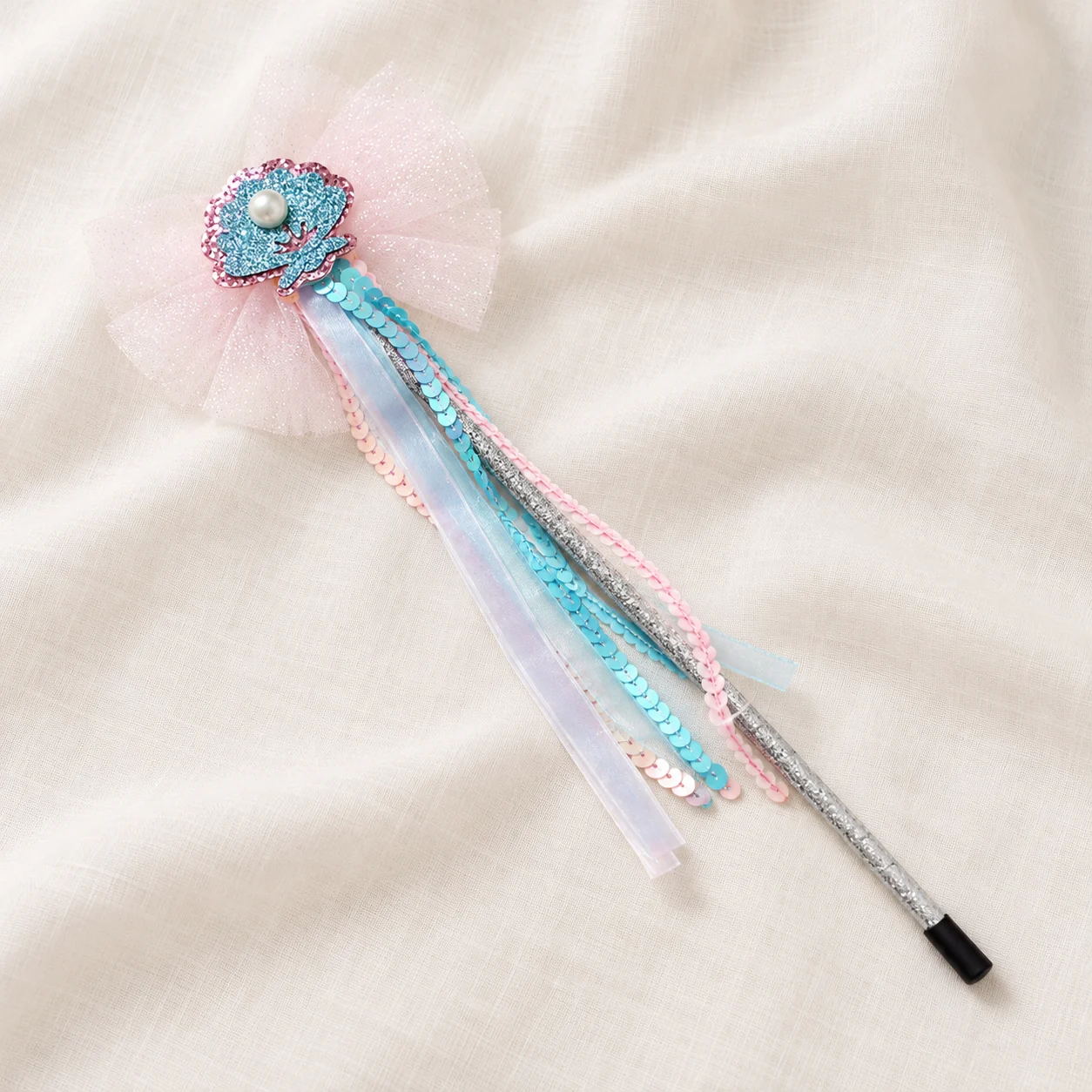 Fairy wand with a sequin shell and ribbon streamers lying on cream silk