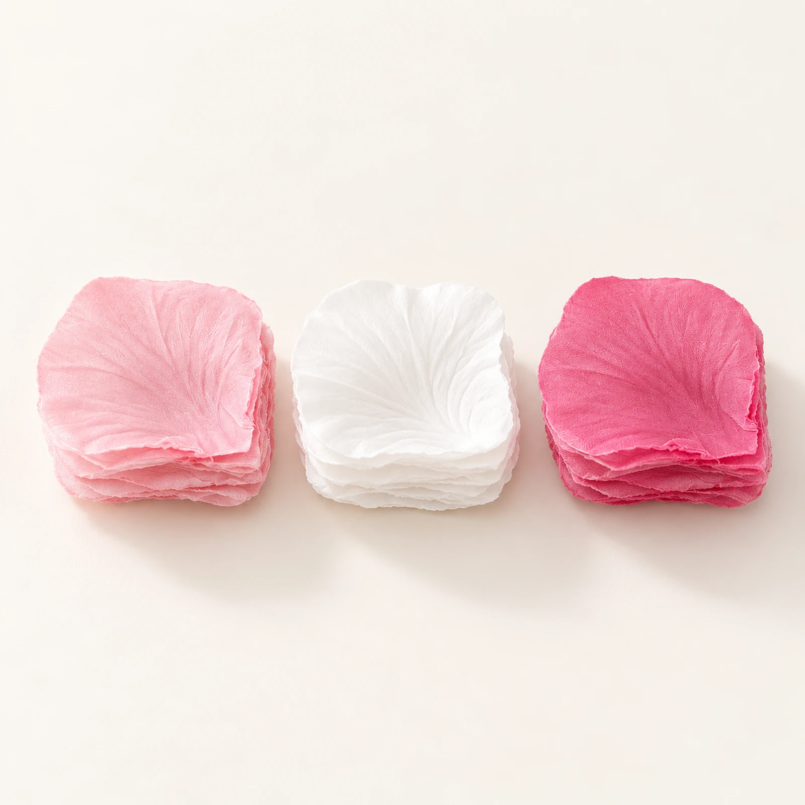 Three stacks of fabric flower petals in blush pink, white and deep rose