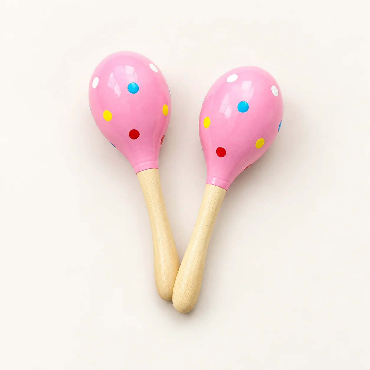 A pair of pink painted wooden hand shakers with colorful dots and natural wood handles