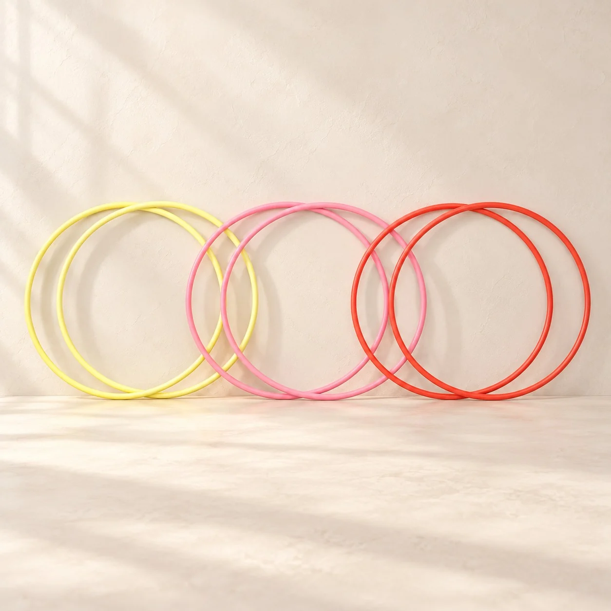 Six jump hoops in yellow, pink and red standing in pairs against a cream wall